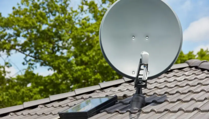 Antena satelitarna na dachu, obok okna dachowego. Prawidłowe ustawienie to klucz do tego, jak poprawić jakość sygnału satelitarnego.