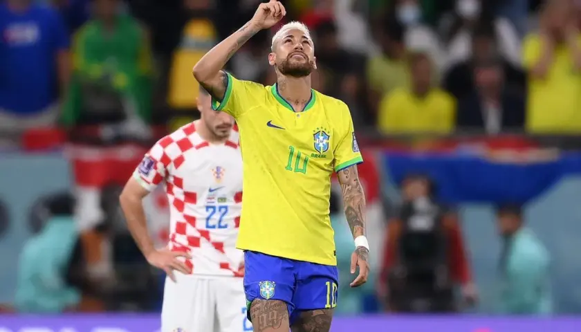Neymar w żółtej koszulce Brazylii z podniesionym palcem, na tle stadionu.