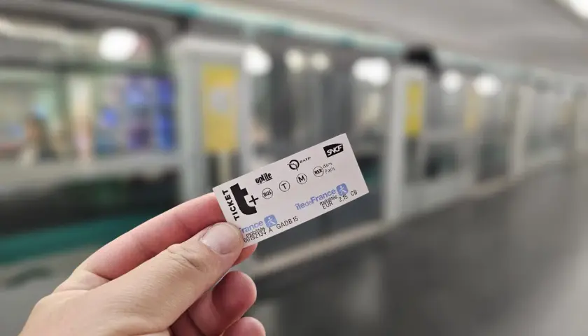 Dłoń trzyma bilet na metro paryskie. W tle widać pociąg metra.