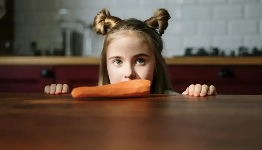 Bambina con acconciatura a ciambella guarda una carota, forse un caso di neofobia alimentare.