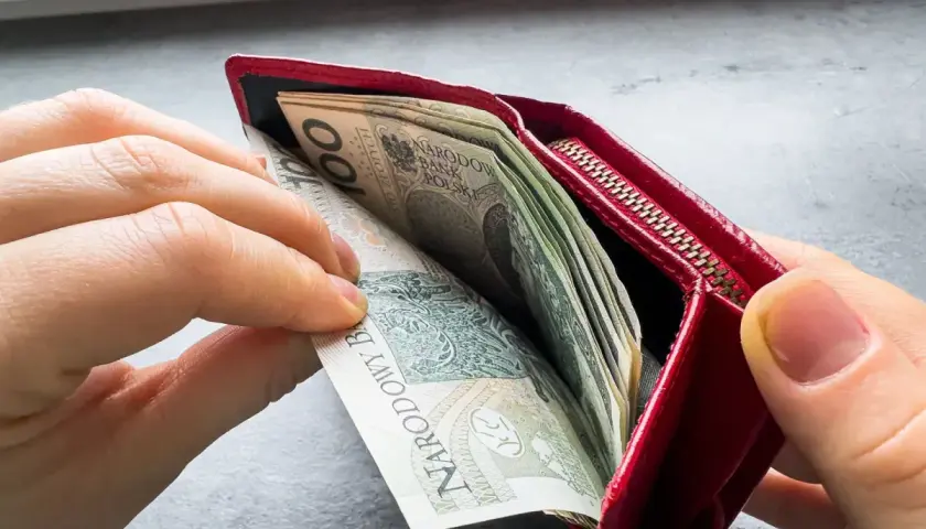 Ręce wkładają pieniądze do czerwonego portfela. To może być symbol wsparcia finansowego, jak zus renta rodzinna po mężu.