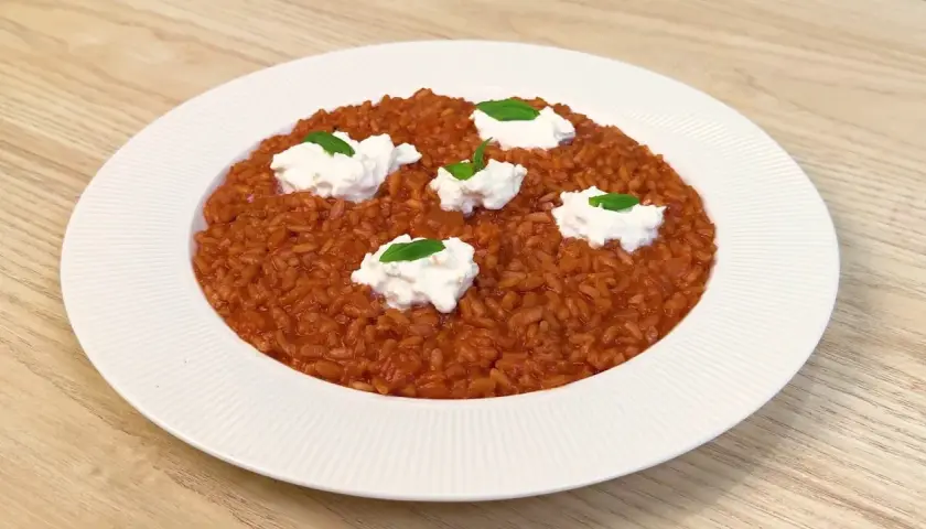 Un invitante risotto al pomodoro, arricchito da ciuffi di ricotta fresca e basilico, pronto per essere gustato.
