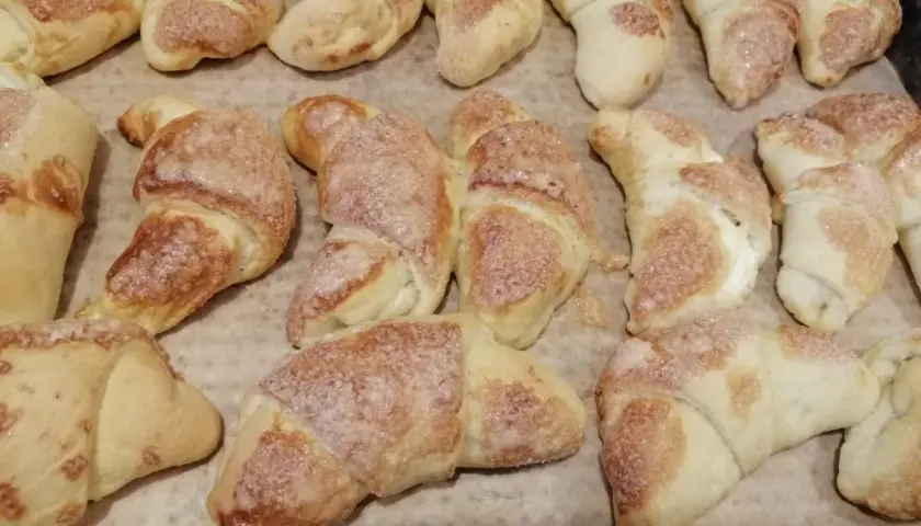 Rogaliki z masą serową, posypane cukrem, pieczone na papierze.