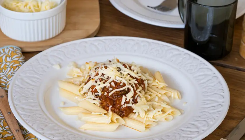 Macarrones con carne picada, cubiertos de queso rallado, servidos en un plato blanco con un diseño floral.