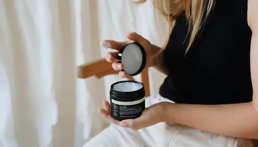 Kobieta z blond włosami kręconymi otwiera słoiczek z maską do włosów.