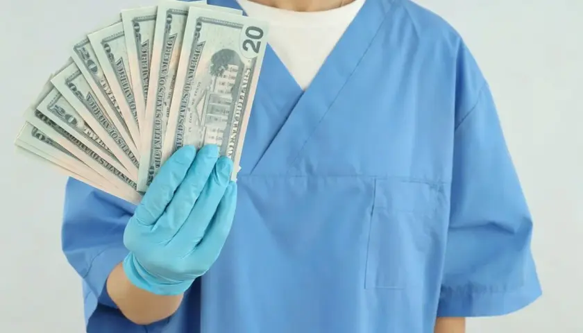 Higienistka stomatologiczna w niebieskim fartuchu pokazuje banknoty dwudziestodolarowe. Zastanawiasz się, ile zarabia higienistka stomatologiczna?