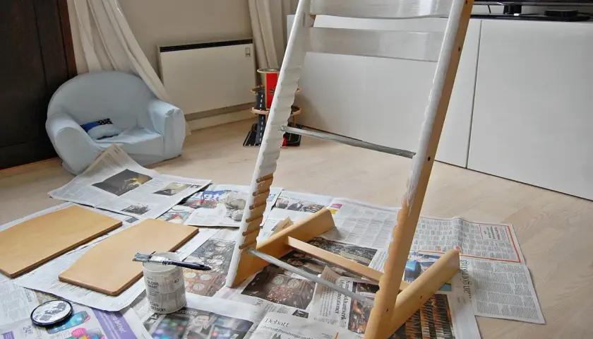 Måla om Stokke stol med vit färg. Trädelar och pensel ligger på tidningspapper.