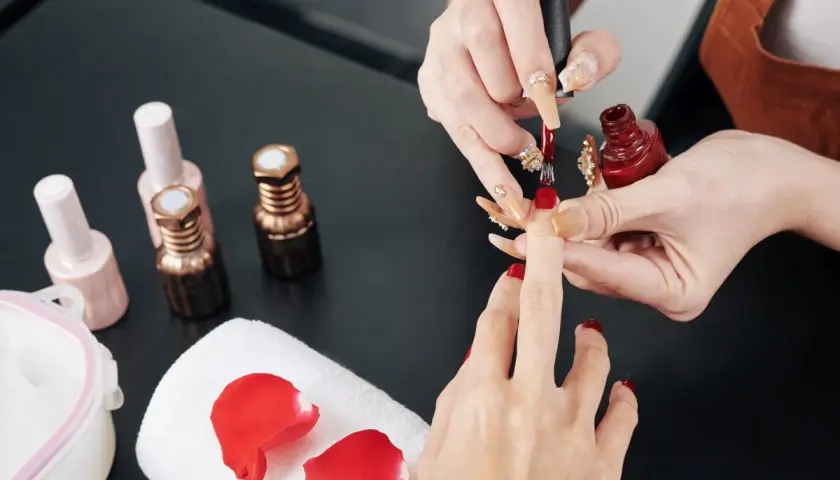Manicure w trakcie. Stylistka nakłada czerwony lakier. Zastanawiasz się, jak przyspieszyć wysychanie lakieru do paznokci?