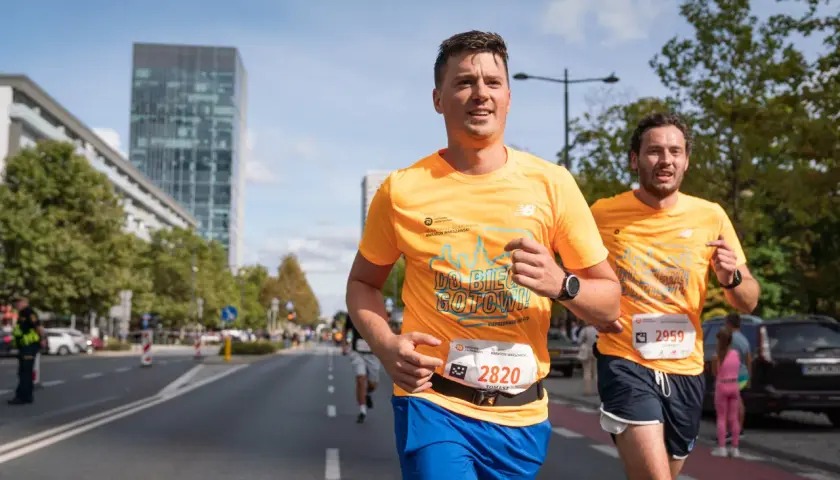 Dwóch biegaczy w pomarańczowych koszulkach na ulicach Warszawy podczas maratonu. Czy to już 42 maraton ile km?