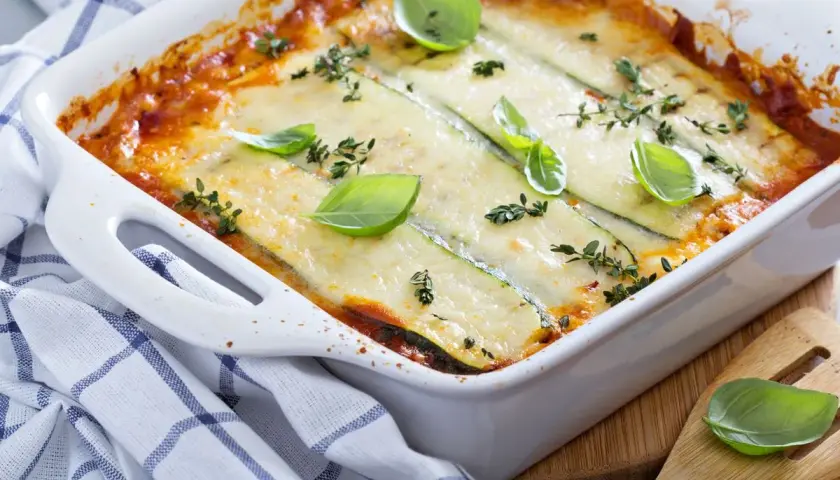 Pasticcio di zucchine appena sfornato, dorato e filante, guarnito con basilico fresco e timo.
