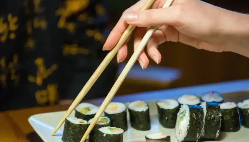 Dłoń z pałeczkami sięga po rolkę sushi. Smaczne i zdrowe, ale warto pamiętać o sushi kcal.