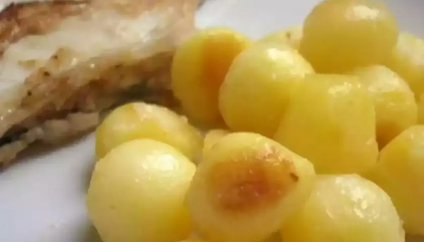 Une assiette de poisson grillé avec une généreuse portion de pomme de terre parisienne, dorée et appétissante.