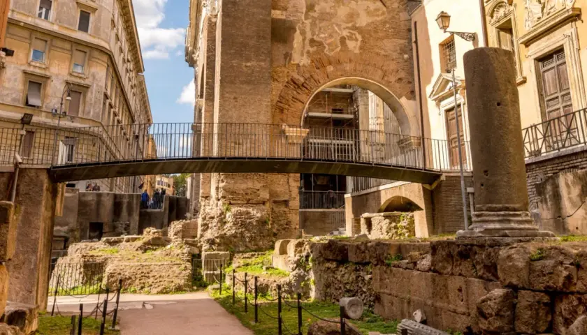 Antiche rovine nel ghetto ebraico di Roma, cosa vedere: un ponte moderno attraversa resti di colonne e mura di mattoni.
