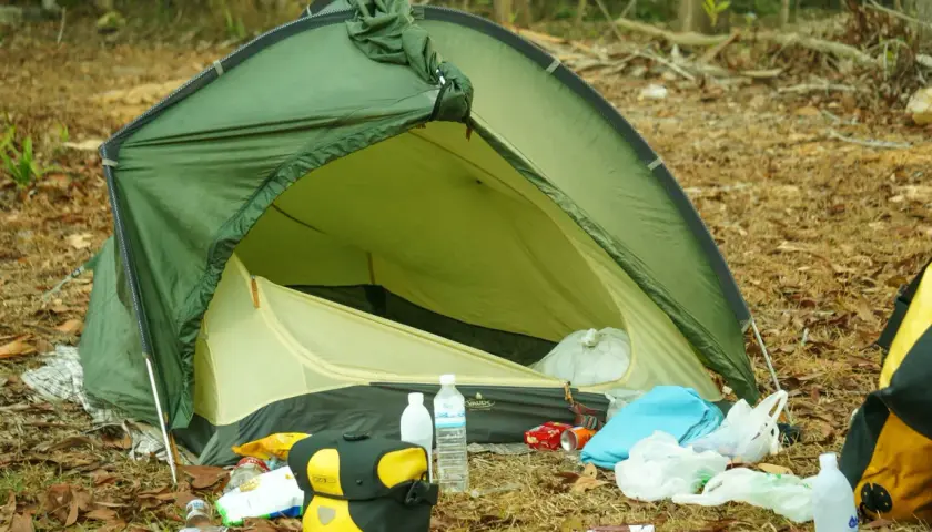 Zielony namiot VAUDE rozbity na leśnej polanie, wokół śmieci. Jaki namiot, taki biwak.
