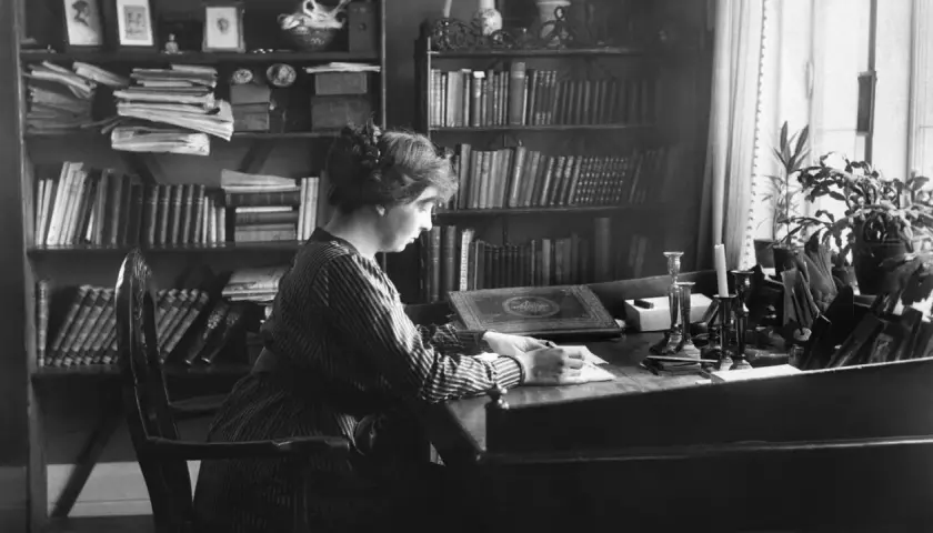 Norwegische Schriftstellerin Sigrid sitzt an ihrem Schreibtisch, umgeben von Büchern, und schreibt.