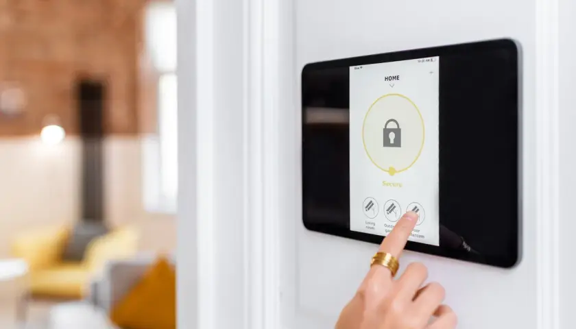 Main d'une personne touchant un écran tactile pour activer un système d'alarme filaire ou sans fil.