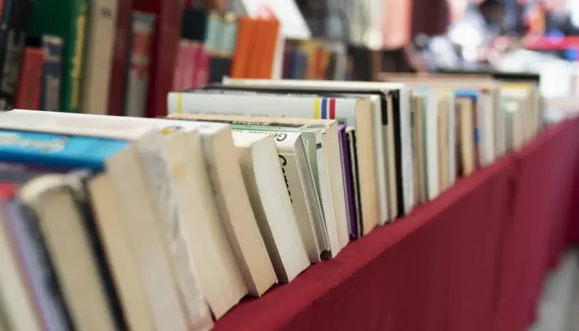 Rząd książek na czerwonym obrusie. Jak przygotować się do targów książki jako autor i czytelnik?