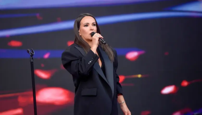 Kasia Kowalska śpiewa na scenie, wykonując swoje utwory w eleganckiej czarnej marynarce.
