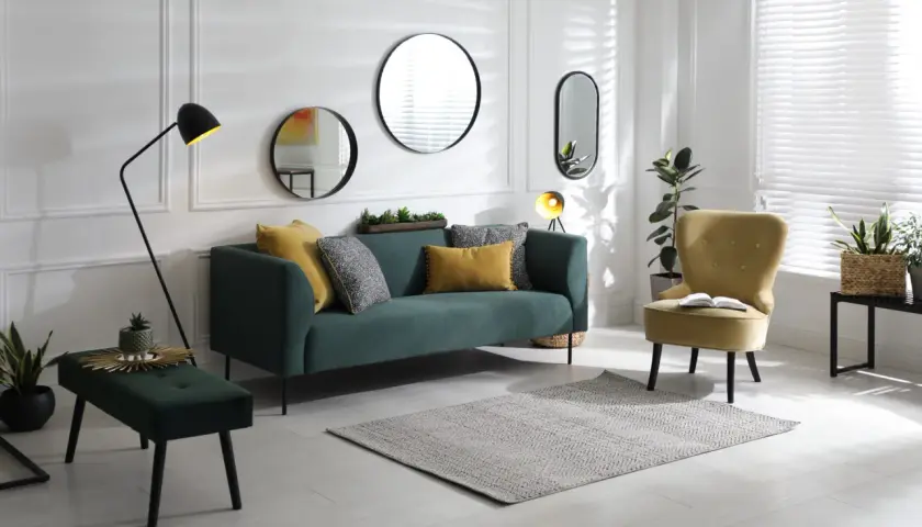 Un salon moderne avec un canapé vert, un fauteuil jaune et plusieurs miroirs derrière le canapé.