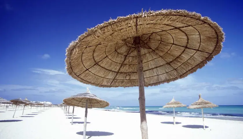 Słomiane parasole na białej plaży, błękitne niebo i morze. Idealna pogoda Tunezja marzec na relaks.