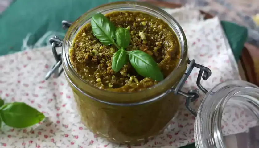 Słoik z pysznym, domowym pesto pistacjowym, ozdobiony listkami bazylii. Idealne do makaronu i kanapek.