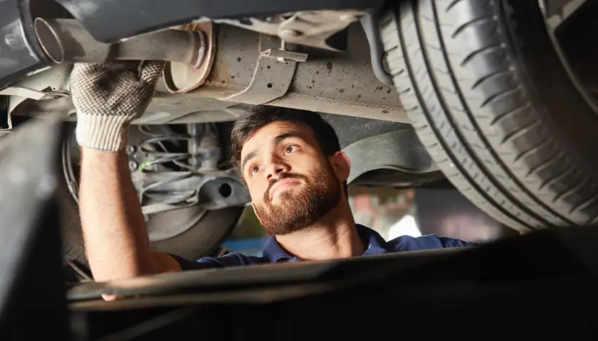 Mechanik w rękawiczce sprawdza podwozie samochodu, wykonując naprawę układu wydechowego.