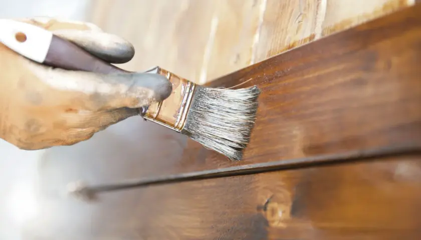 Mano enguantada aplica barniz a madera. El proceso de lijar entre capas de barniz asegura un acabado perfecto.