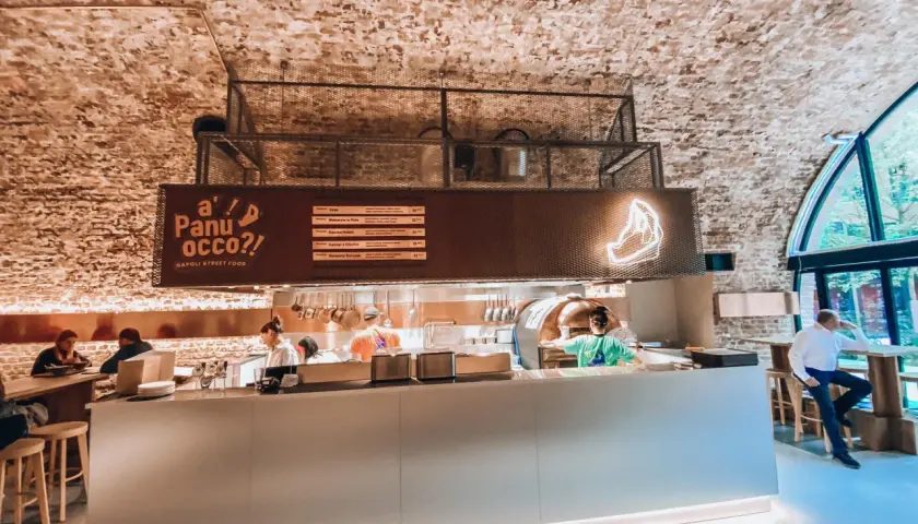 Wnętrze jednej z nowych restauracji w Warszawie. Widać piec do pizzy, bar i gości.