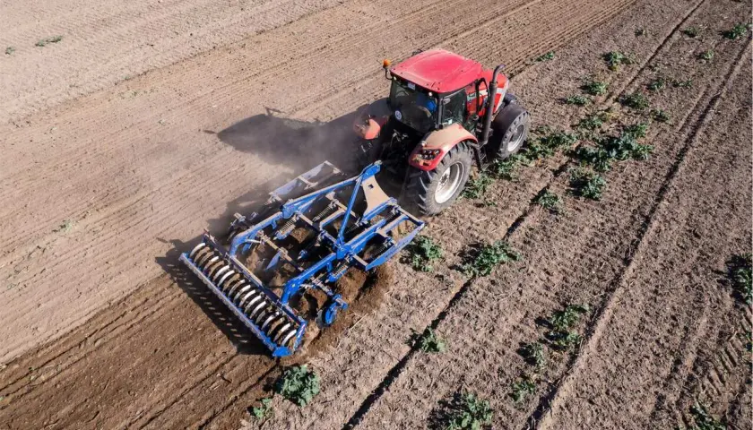 Un tracteur rouge travaille le sol avec un cultivateur, préparant le terrain pour la culture sans labour.