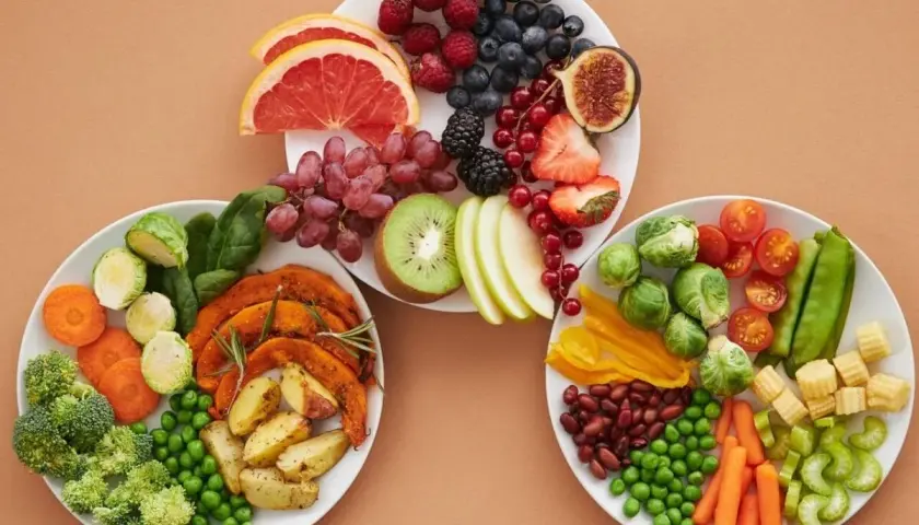Platos con frutas y verduras frescas, incluyendo arándanos, fresas, uvas, kiwi, brócoli, zanahorias y guisantes. Una selección de alimentos diuréticos para una dieta saludable.