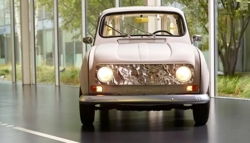 En ljusbeige Renault 16 står framför stora fönster med grönska utanför. Bilens front med sina runda strålkastare och kromade grill är i fokus.
