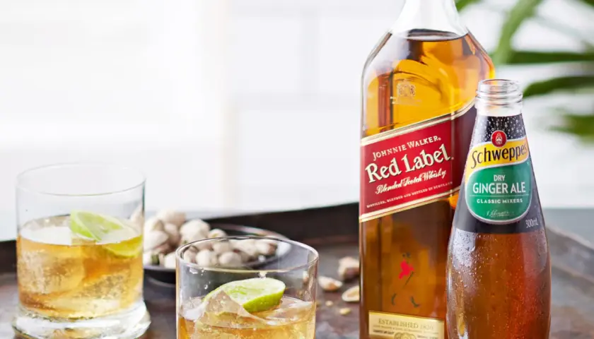 Butelka Johnnie Walker Red Label, butelka Schweppes Ginger Ale i dwa drinki z lodem i limonką.