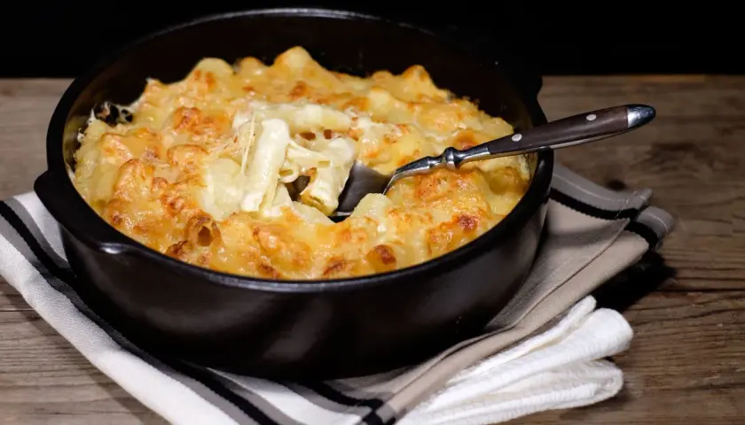 Un plat réconfortant de gratin de pâtes à l'ancienne, doré et gratiné au fromage, servi dans un plat noir avec une cuillère.
