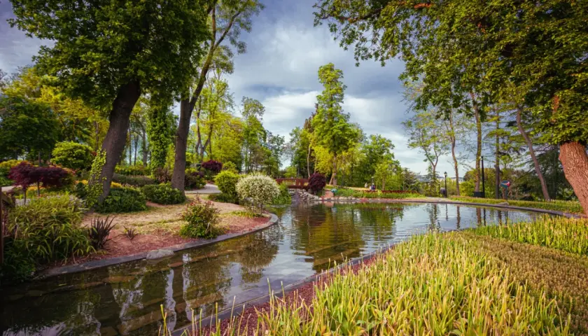 Malowniczy park z jeziorem, mostkiem i bujną zielenią.