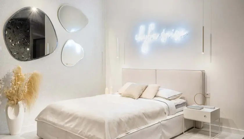 Nowoczesne oświetlenie sypialni inspiracje: neonowy napis, wiszące lampy i lustra o organicznych kształtach tworzą przytulną atmosferę.