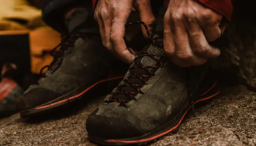 Hands tying red-laced hiking boots. Proper fit is crucial for comfort and performance on the trail.
