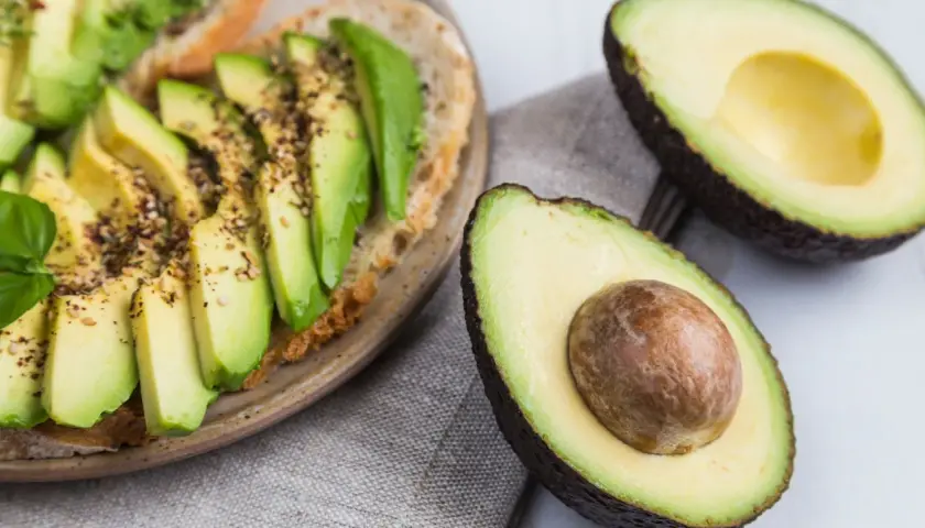 Avocado-Toast mit Gewürzen und frischem Basilikum. Ist Avocado Obst oder Gemüse? Botanisch ist sie eine Frucht, kulinarisch oft als Gemüse verwendet.