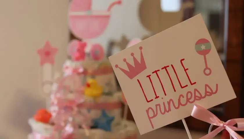 Urocza dekoracja na baby shower z napisem "Little princess", koroną i grzechotką. W tle tort z pieluch i różowa karoca. Prawdziwy mały **gwiazdor**!