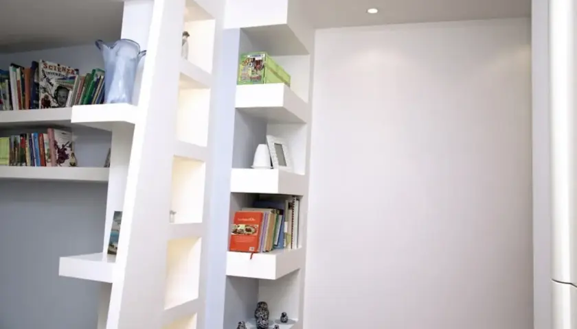 Scaffali moderni in cartongesso, con libri, vasi e soprammobili, creano un angolo lettura accogliente.
