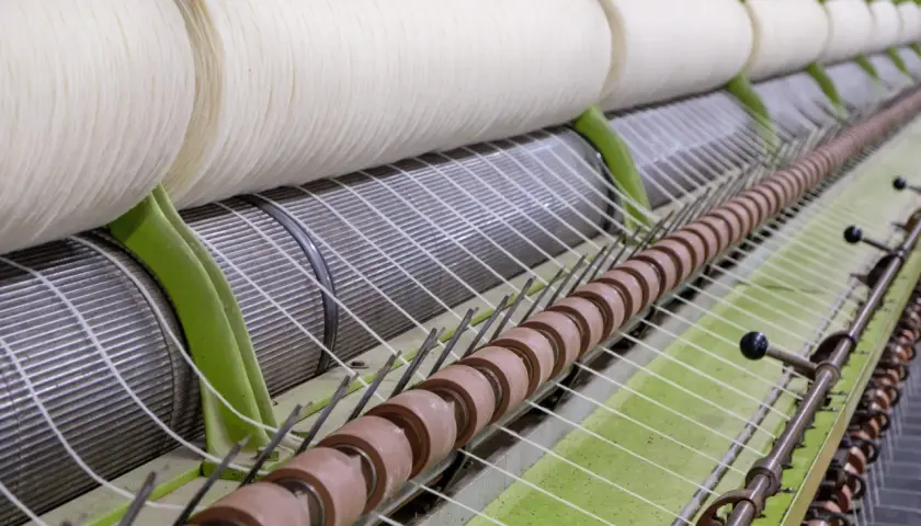 Gros rouleaux de fil blanc sur une machine de filature. Le processus de filature est en cours, transformant la matière première en fil.