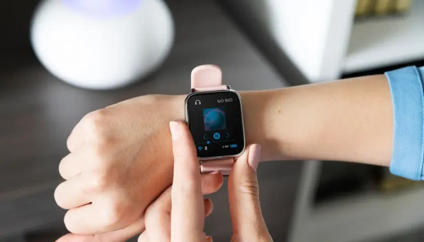 Różowy smartwatch na nadgarstku pokazuje ekran odtwarzania muzyki. Dowiedz się, jak sparować zegarek z telefonem, by cieszyć się ulubionymi utworami.