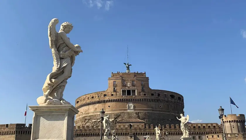 Un angelo scolpito domina la scena davanti al maestoso mausoleo di Roma, Castel Sant'Angelo, sotto un cielo azzurro.