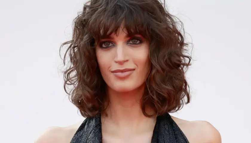 Mujer con curly pelo corto rizado natural, mirada intensa y vestido negro brillante.