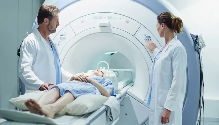 Pacjentka na stole do rezonansu magnetycznego, lekarze nadzorują badanie. Sprawdź rezonans magnetyczny - cennik usług medycznych.