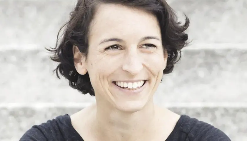 Lachende Frau mit kurzen Haaren, die an Madame Moneypenny Kritik erinnert.