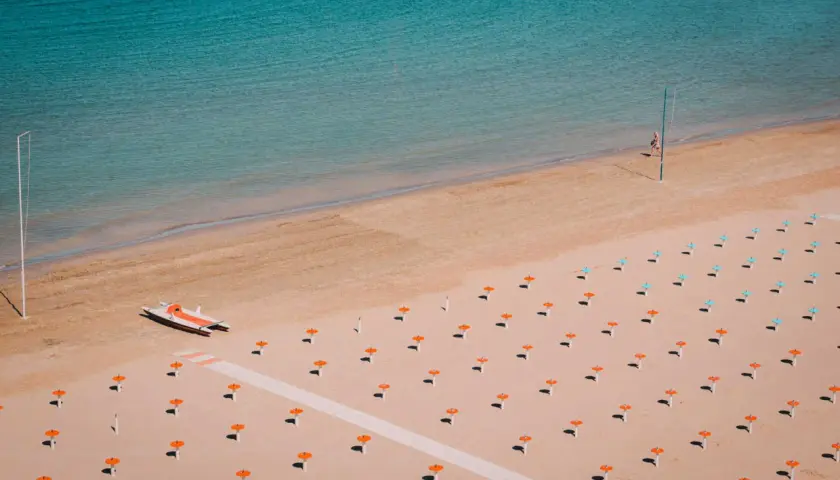 Pusta plaża w Rimini z rzędem pomarańczowych parasoli i małą łodzią motorową.