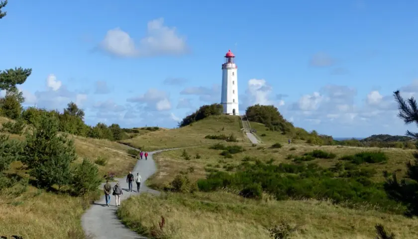 Ein Hiddensee Tagesausflug führt über grasbewachsene Hügel zum Leuchtturm. Wanderer genießen die sonnige Aussicht.