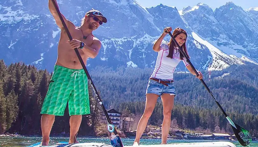 Ein Mann und eine Frau genießen das Stand Up Paddle Boarding auf einem Bergsee.