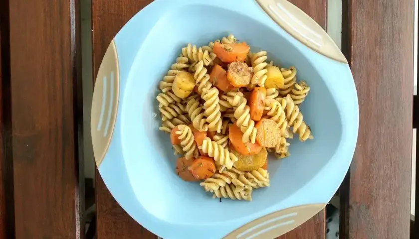 Makaron fusilli z marchewką i ziemniakami na niebieskim talerzyku.