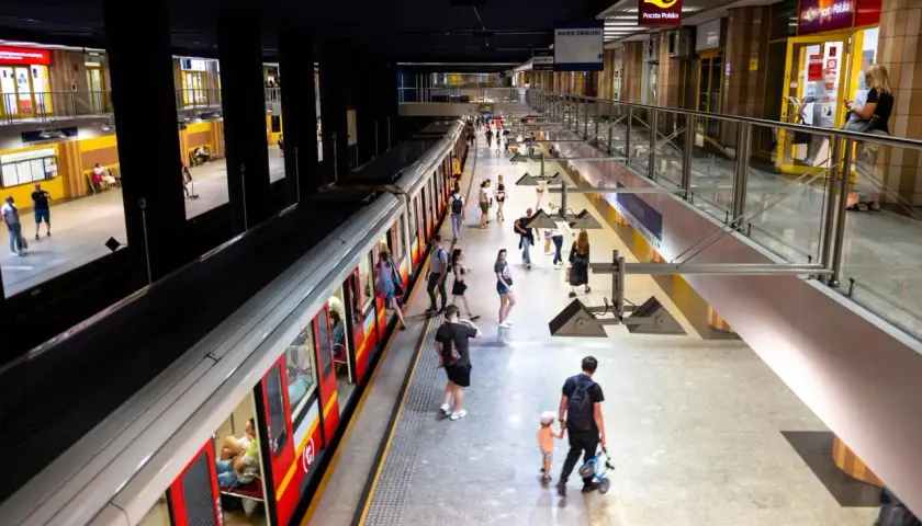 Ludzie na peronie metra, szukający drogi z dworca centralnego do metra. Widać pociąg i wejścia do sklepów.